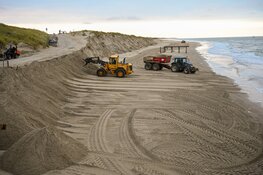 Trekkers en shovels aan het werk om weggeslagen zand te herstellen