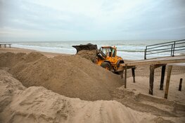 Trekkers en shovels aan het werk om weggeslagen zand te herstellen